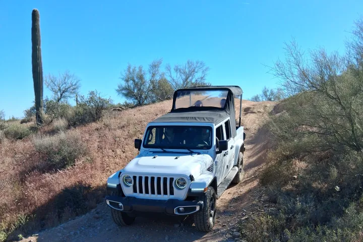 White Jeep on rocky desert trail under clear blue sky.