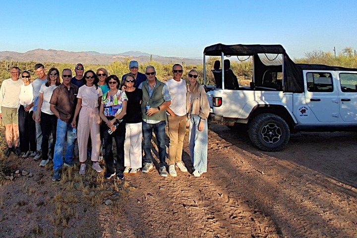 Group of people posing by an off-road vehicle in a desert landscape.
