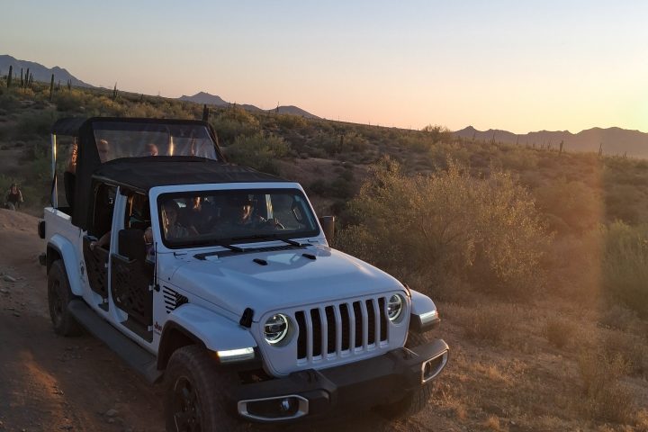 Off-road vehicle on a dirt path at sunset in a desert landscape.