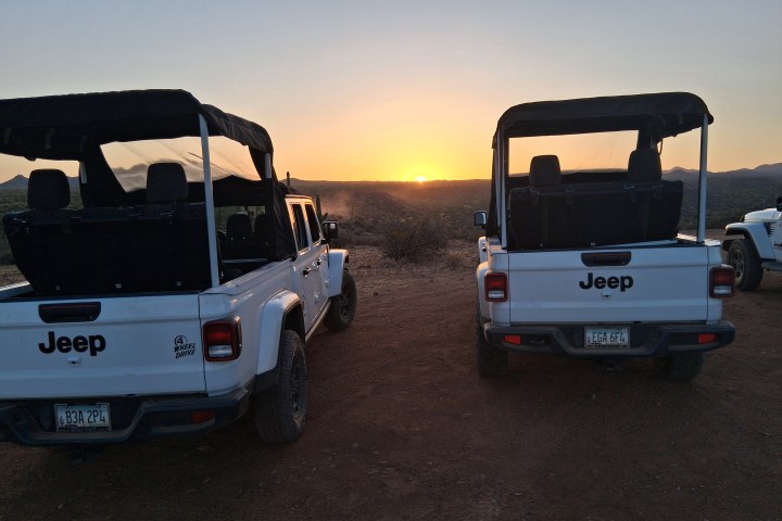 Two white Jeeps parked on dirt road at sunset.