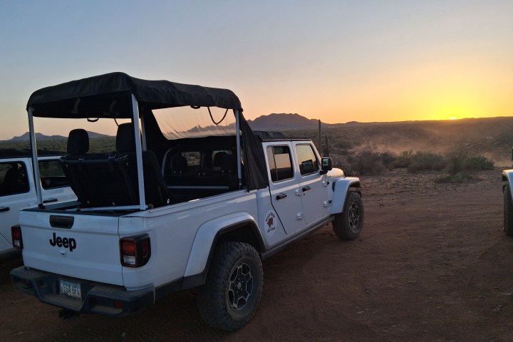 White Jeep parked on a dirt road at sunset.