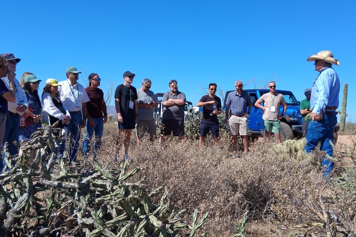 Group of people listening to a speaker outdoors in a desert setting.