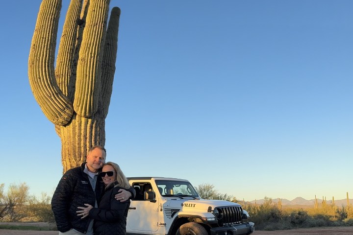 Couple hugging near a large cactus with a white Jeep in the background.