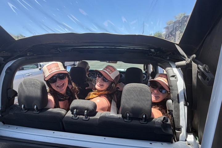 Three smiling people in sunglasses, sitting in a convertible car.