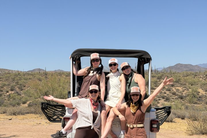 Group posing joyfully on a parked Jeep in desert landscape.
