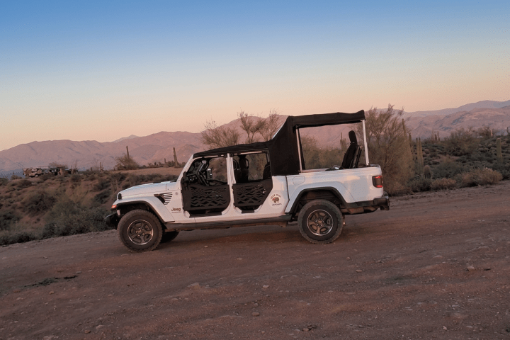 White Jeep with no doors on dirt road at sunset, desert landscape.