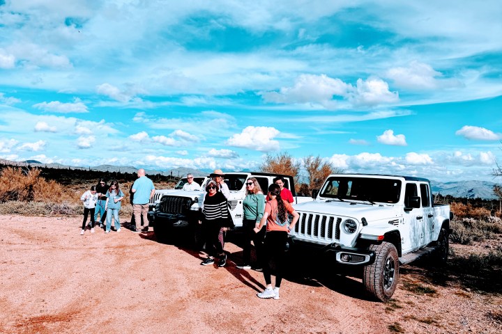 People standing by two white Jeeps in a desert landscape under a bright blue sky.