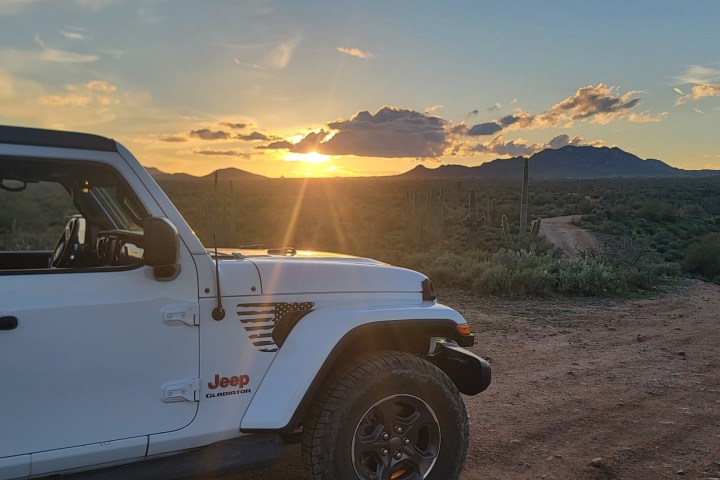 White Jeep parked on a dirt road at sunset with mountains in the background.
