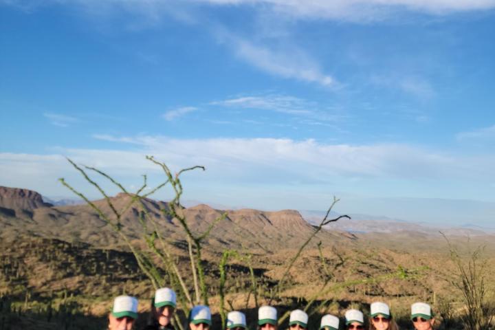 Group of people in hats standing in a desert landscape with mountains in the background.