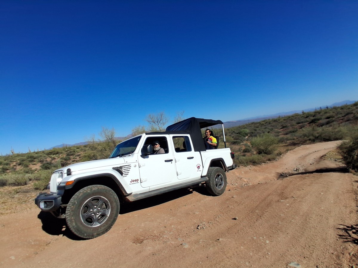 White Jeep on a dirt trail in a desert landscape under a clear blue sky.